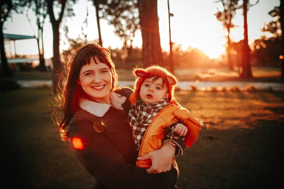 A mother smiling with her awake toddler in golden-hour light