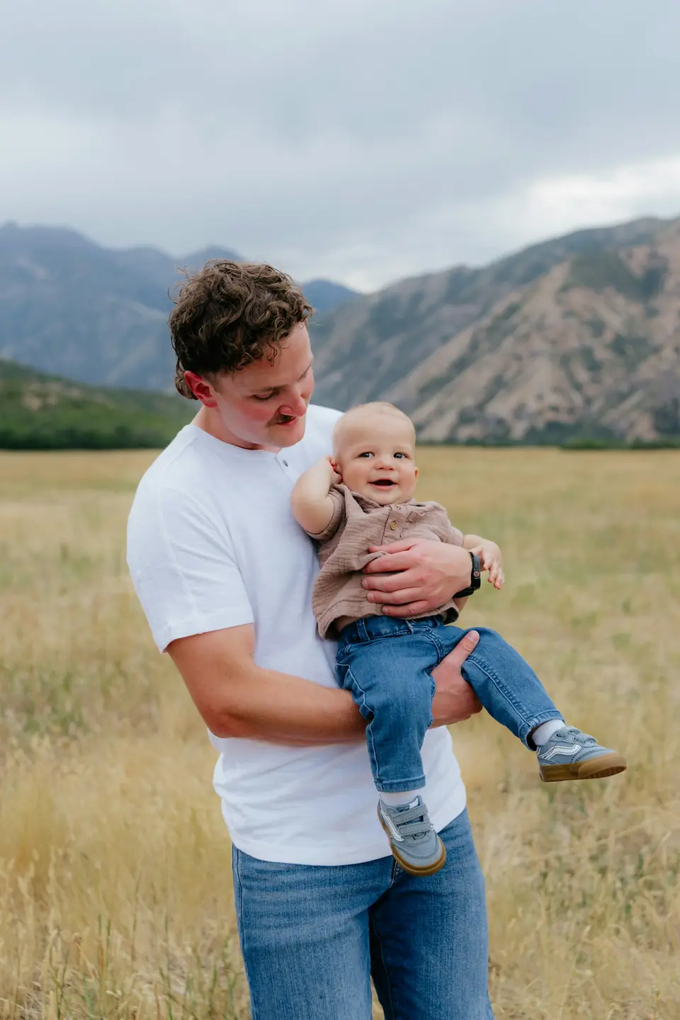 A father holding his smiling baby in a mountain field
