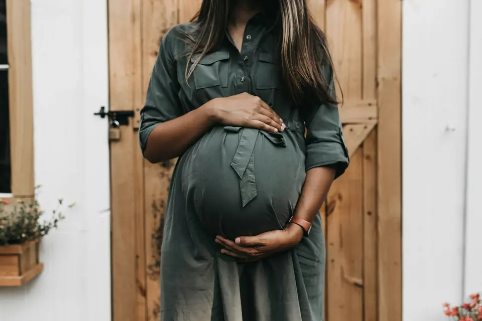 A pregnant woman in a green dress holding her belly