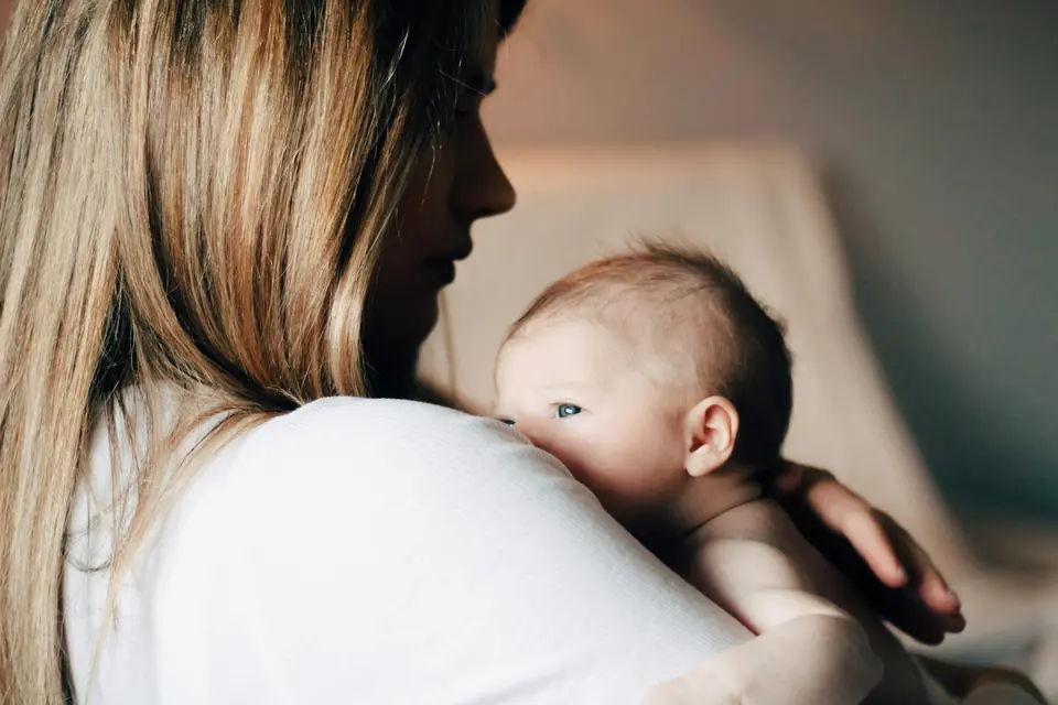 A baby looking over his mother's shoulder as she holds him