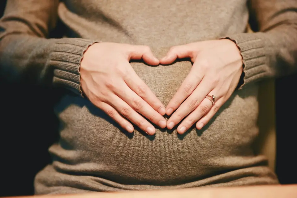 Hands making a heart shape over a small bump