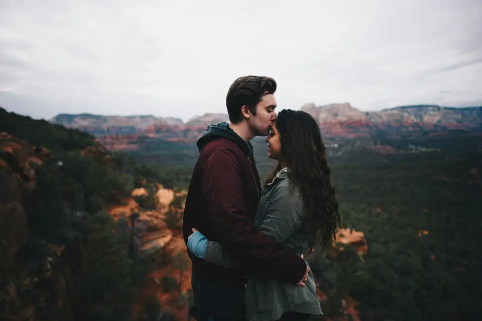 A man kissing a woman's forehead above a canyon