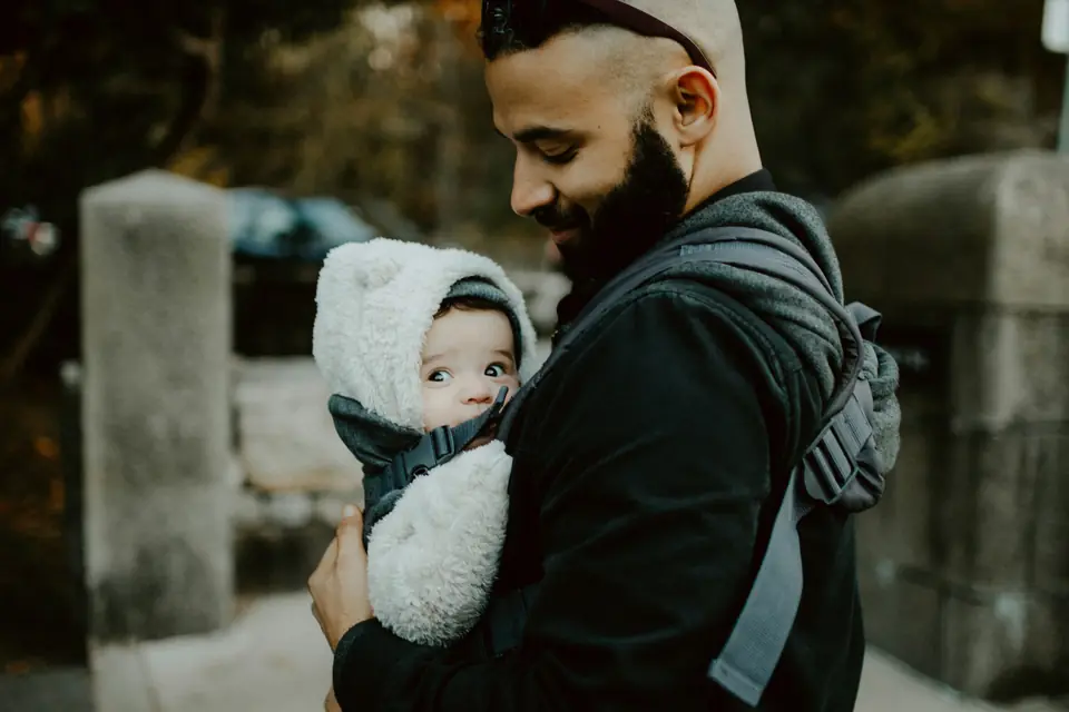 A father carrying his infant in a soft structured carrier, candid outdoor shot