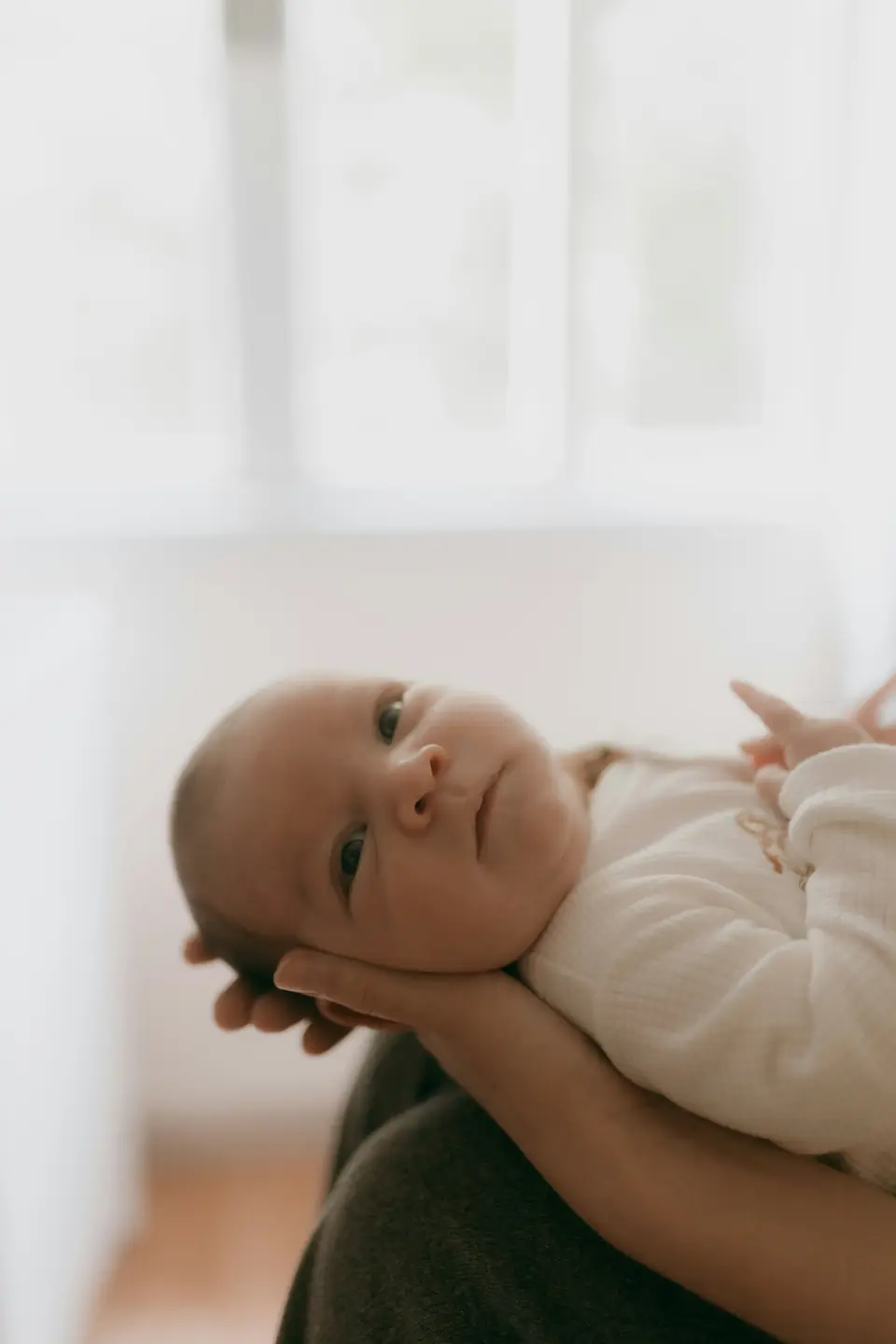 A wide-eyed, clearly awake baby held by an adult in warm daylight