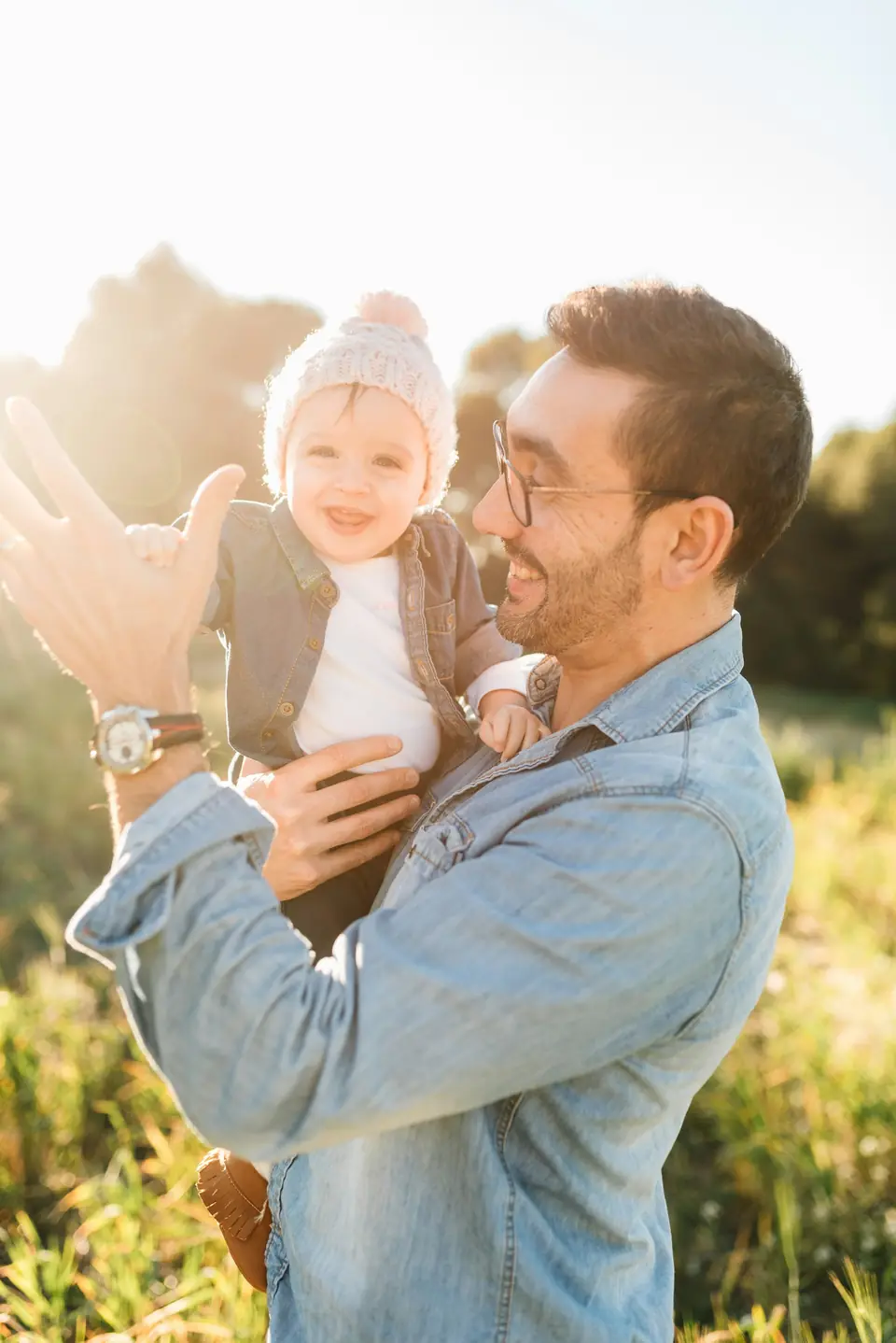 A father holding a smiling baby in a sunny field