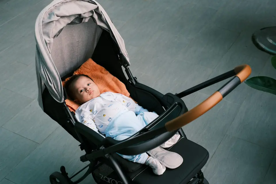 A baby lying awake in a black stroller under a grey canopy, looking up toward the camera
