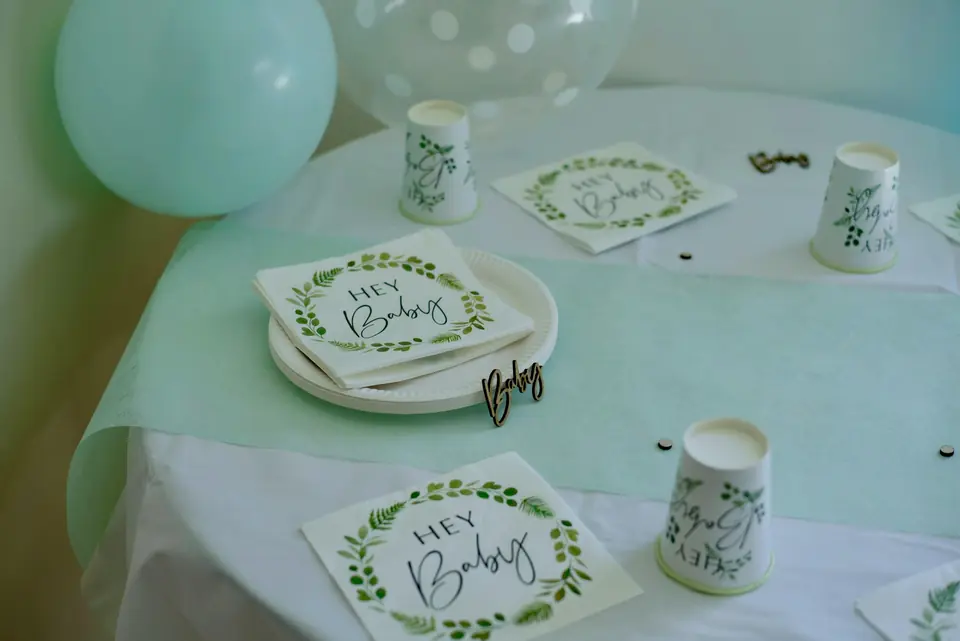 A baby shower gift table with "Hey Baby" napkins and cups, balloons, and confetti