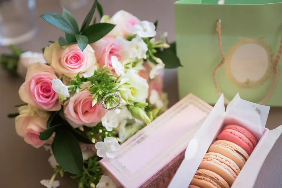 Pink and cream rose bouquet with a ring nestled in it, beside a box of macarons