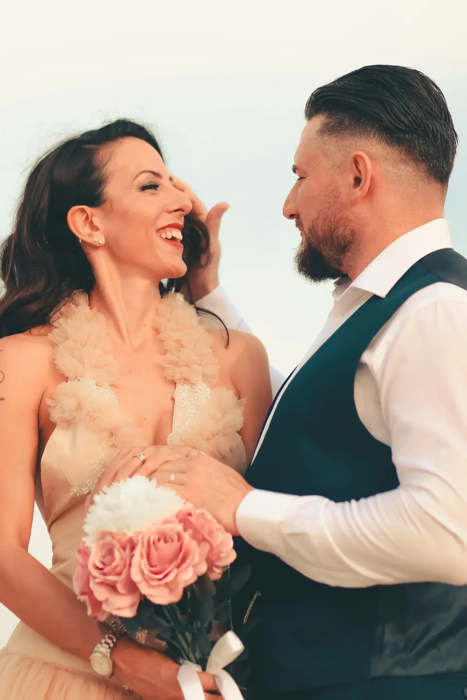 A bride holding pink roses, laughing with her groom