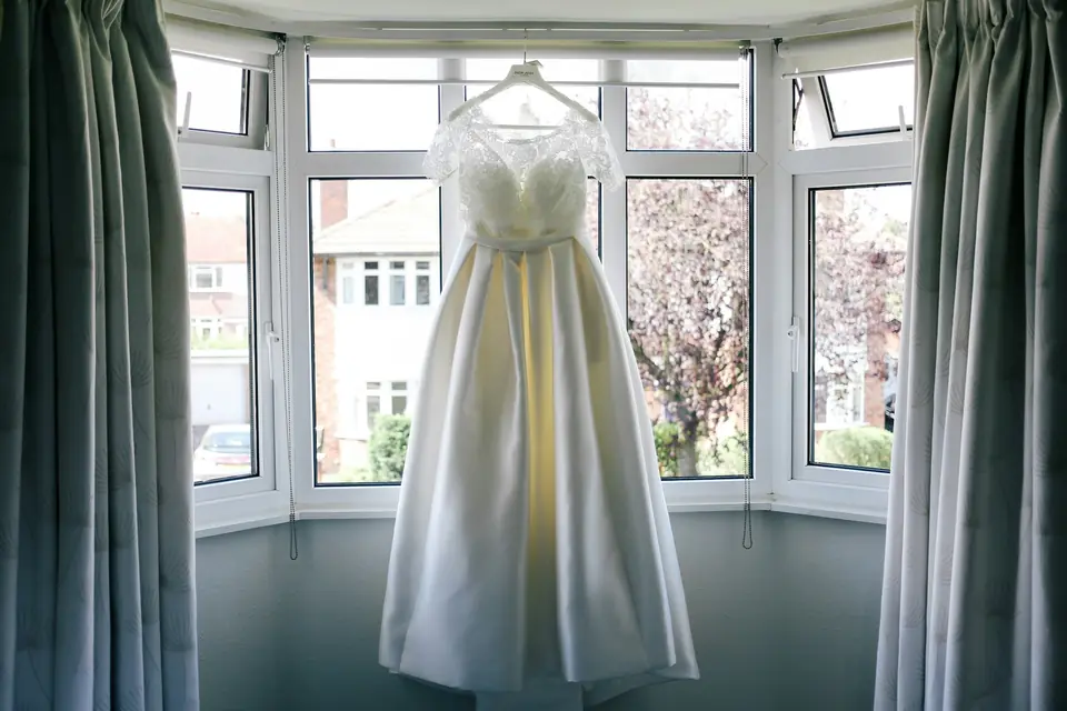 A white sleeveless wedding gown displayed near a window